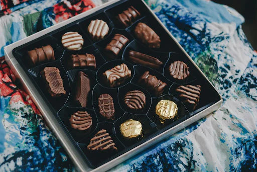 Assorted box of chocolates with different shapes and designs, including wrapped gold pieces.