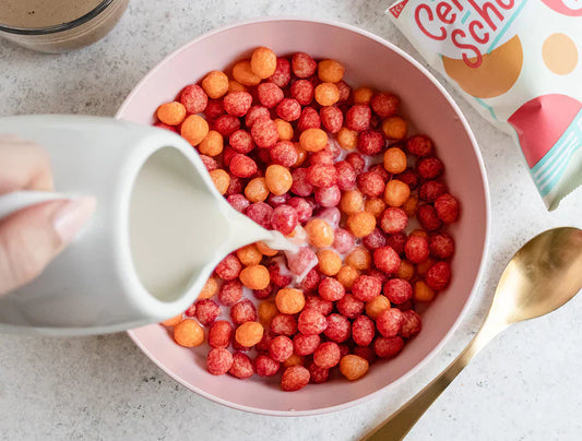 Milk being poured into a bowl of Schoolyard Snacks fruity cereal with a gold spoon beside it.