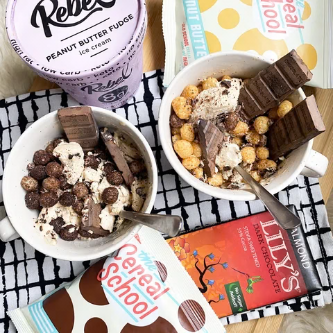 Bowls of Schoolyard Snacks keto cereal topped with Rebel ice cream, Lily’s dark chocolate, and candy bars.